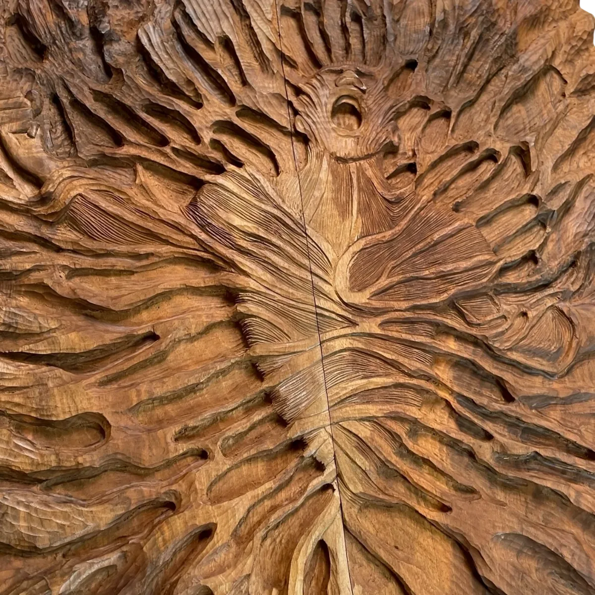 Close-up of the carved human figure: an open-mouthed face surrounded by flame-like curves