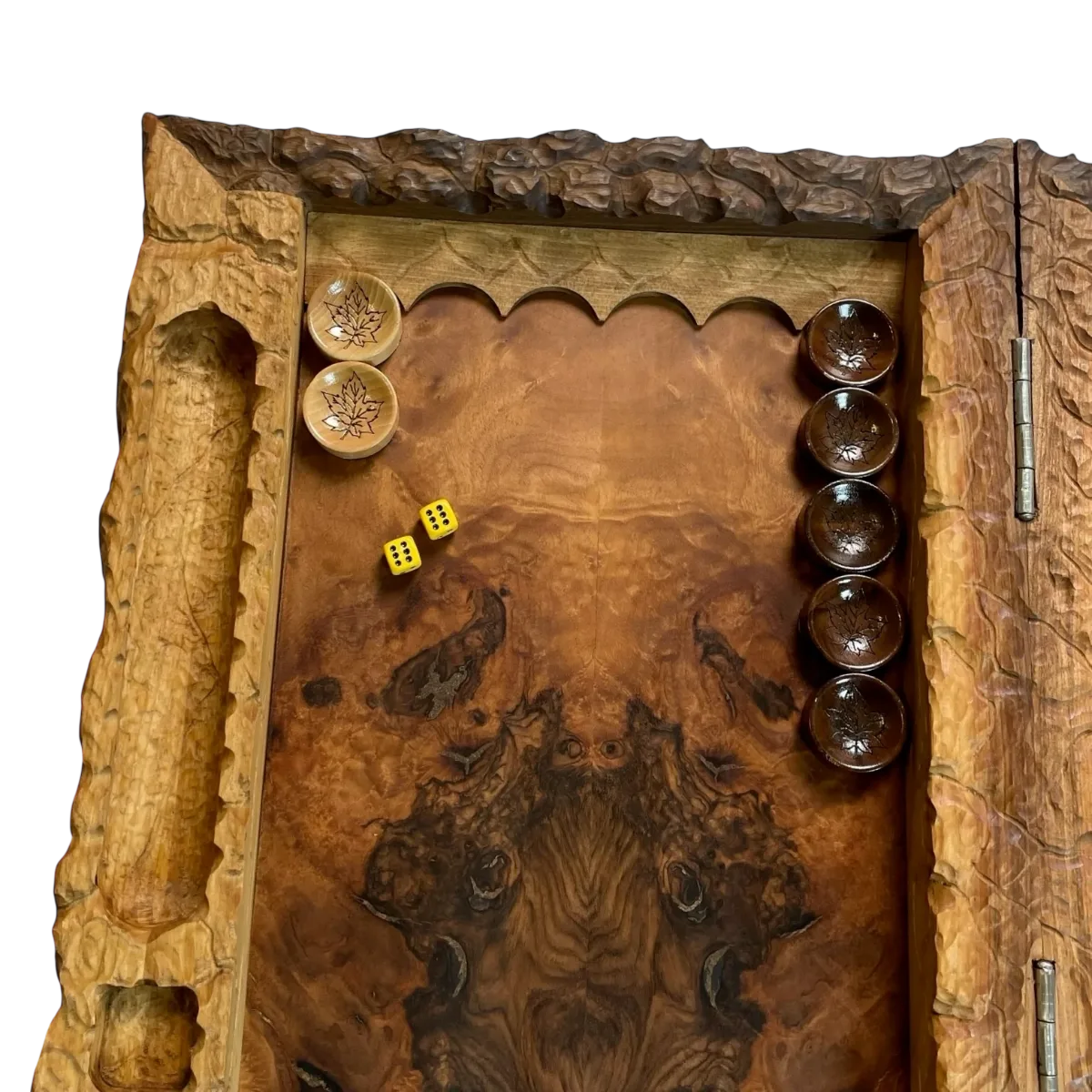 Corner of an open carved backgammon board: grained playing surface, light and dark leaf-motif checkers, two yellow dice and hinges